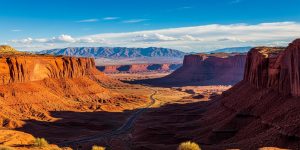 A scenic desert highway winds through red sandstone canyon formations glowing in golden morning light near Las Vegas, Nevada, capturing the breathtaking landscape of a day trip from the city toward destinations like Red Rock Canyon or Valley of Fire.
