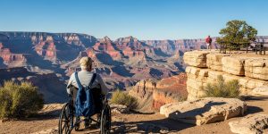 A senior man in his 70s in a wheelchair at Mather Point on the Grand Canyon South Rim, gazing at the breathtaking canyon vista on an accessible Grand Canyon tour from Las Vegas, with smooth paved paths and benches visible nearby.