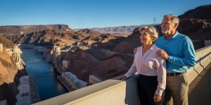 A senior couple in their 60s on the pedestrian walkway of the Memorial Bridge overlooking Hoover Dam and the Colorado River in Nevada, enjoying the dramatic canyon scenery on a Hoover Dam tour from Las Vegas in the early morning light.