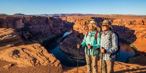 A senior couple in their 60s standing at the Horseshoe Bend overlook near Page, Arizona, admiring the sweeping Colorado River curve below on a Las Vegas to Page Arizona road trip for seniors in 2026, with dramatic canyon walls and clear desert sky behind them.