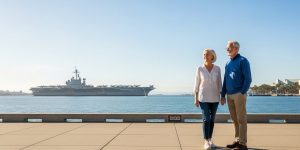 A senior couple in their 60s enjoying the accessible San Diego waterfront Embarcadero with the USS Midway Museum visible behind them, representing why San Diego is the better road trip choice than Los Angeles for Las Vegas seniors in 2026.